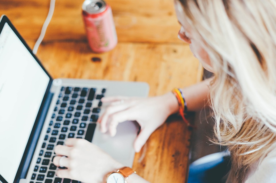 Woman with blond hair typing on a laptop. View from over her left shoulder.