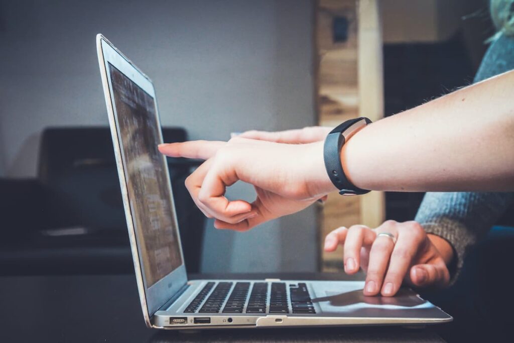 Two hands pointing at a spot on a propped open laptop screen.